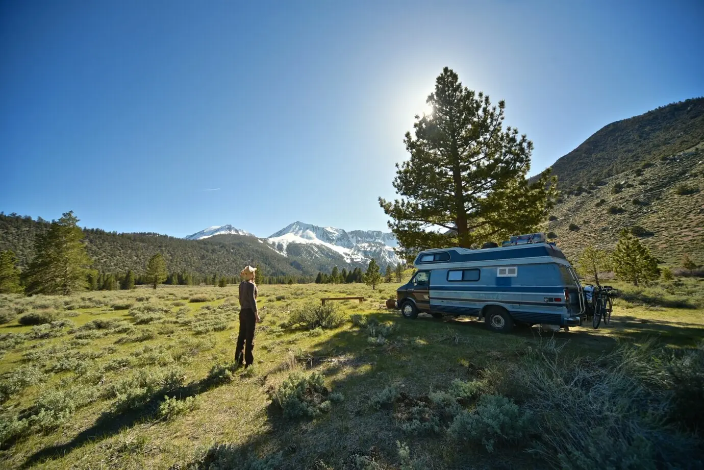 A beautiful photograph of a female standing on a grassy field near a van, with a mountain.
